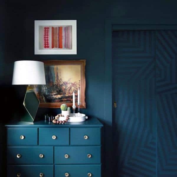 Dark teal room featuring a teal dresser, lamp, and framed art, with a closet door showcasing a geometric pattern