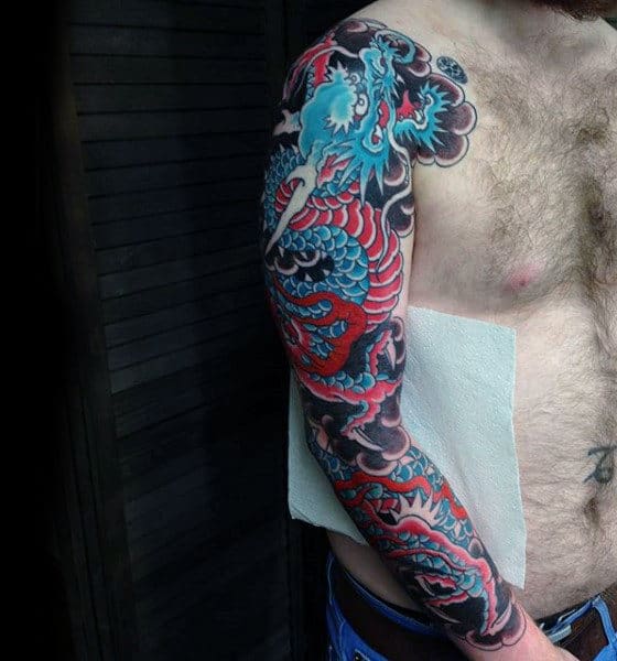 Man's arm with a vibrant dragon tattoo in red, blue, and black ink