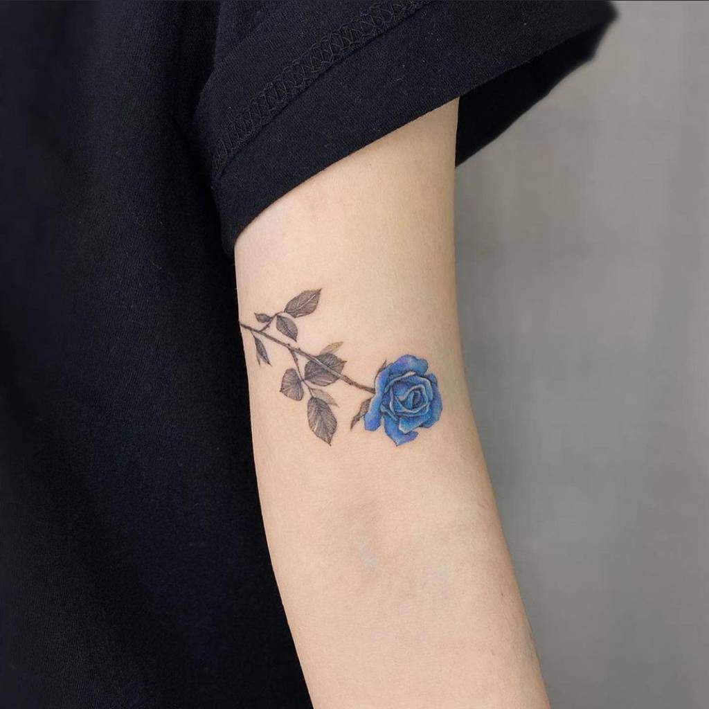 Minimalist sister tattoo featuring a detailed black and gray stem with leaves and a vibrant blue rose in full bloom