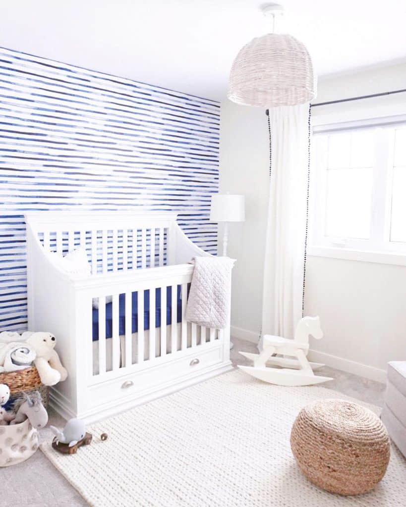 Bright nursery with white crib, blue striped accent wall, and soft neutral decor.