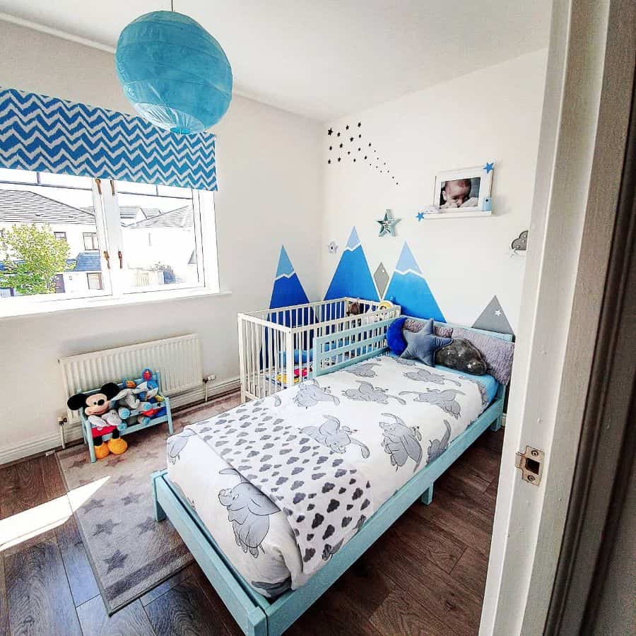 Playful kids' bedroom with blue mountain wall mural, blue bed, and matching decor.
