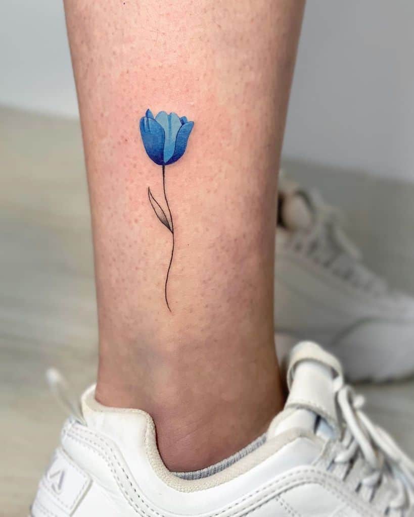 A small, blue tulip tattoo above the ankle on a leg