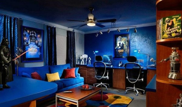 A sci-fi themed room with blue decor, action figures, posters, a blue couch, and a gaming setup with two chairs
