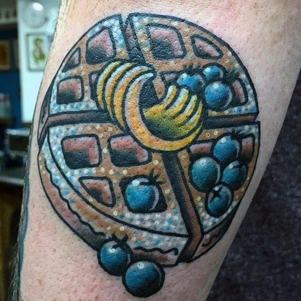 Detailed waffle tattoo featuring a round golden waffle topped with blueberries, banana slices, and syrup, creating a bold and appetizing design.