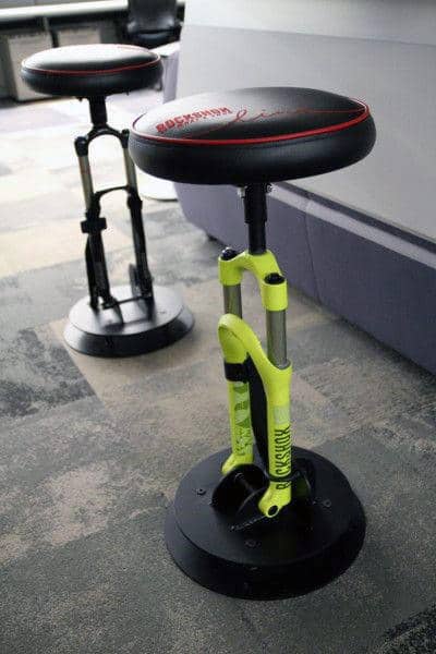 Two unique stools with cushioned seats and bicycle shock absorber bases on a carpeted floor