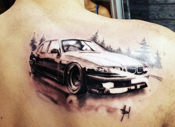 A detailed BMW car tattoo on a shoulder blade featuring a black and white realistic depiction of a car in motion