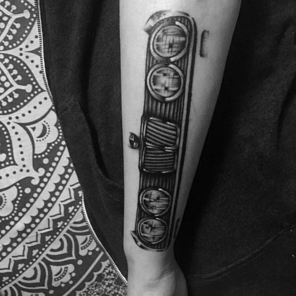 Realistic BMW front grille and headlights tattoo on forearm, detailed in black and grey shading for a bold automotive look.