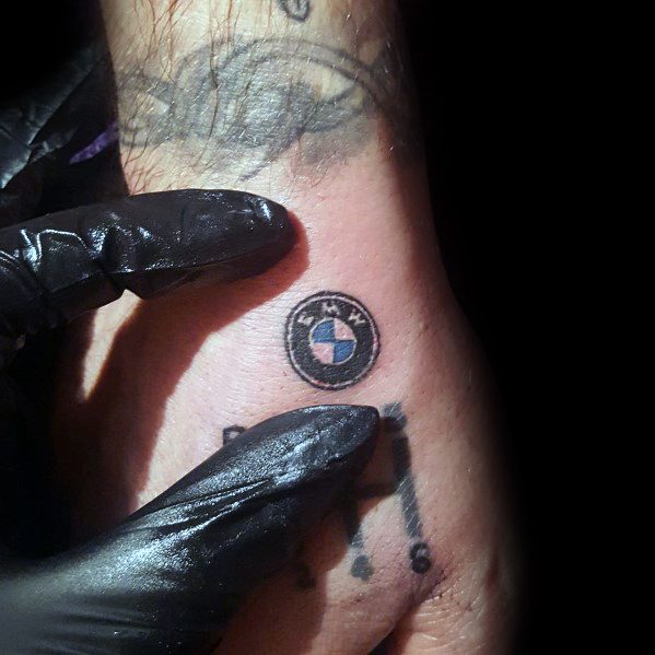 Small BMW logo and gear shift pattern tattoo on hand, featuring minimalistic design for a subtle yet bold automotive statement.