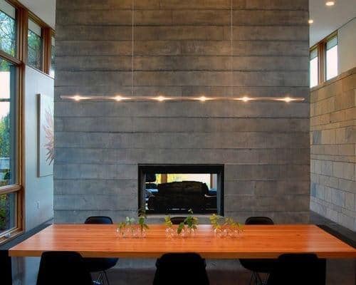 Board-formed concrete fireplace in a modern dining room with a wooden table and sleek lighting.