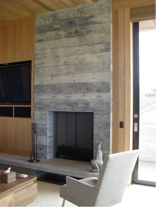 Board-formed concrete fireplace in a cozy living room with wooden walls and neutral furniture.