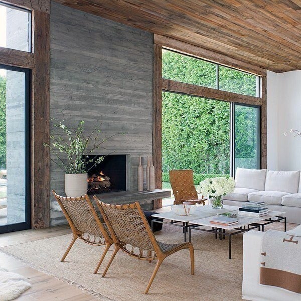 Living room with board-formed concrete fireplace, rustic wood beams, and modern woven chairs.