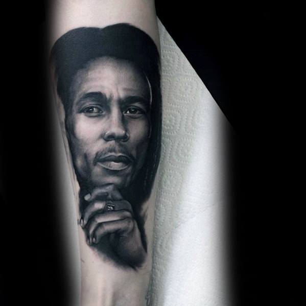 Realistic forearm tattoo of Bob Marley with a contemplative expression, detailed shading capturing his face resting on his hand.