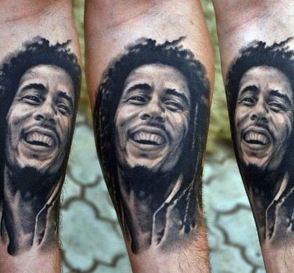 Realistic black and gray tattoo of Bob Marley smiling, placed on the forearm with detailed shading and expressive features.