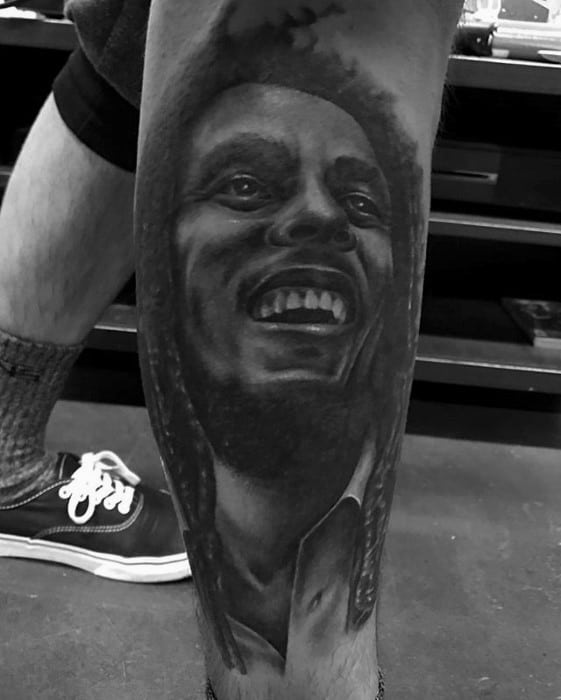 Black and gray leg tattoo of Bob Marley smiling joyfully, with fine detail in the facial features and subtle shading for depth.