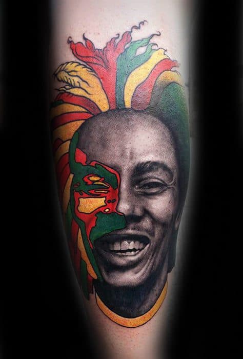 Striking Bob Marley tattoo with half his face in realistic black and gray and the other half in bold red, yellow, and green tribal-style design.