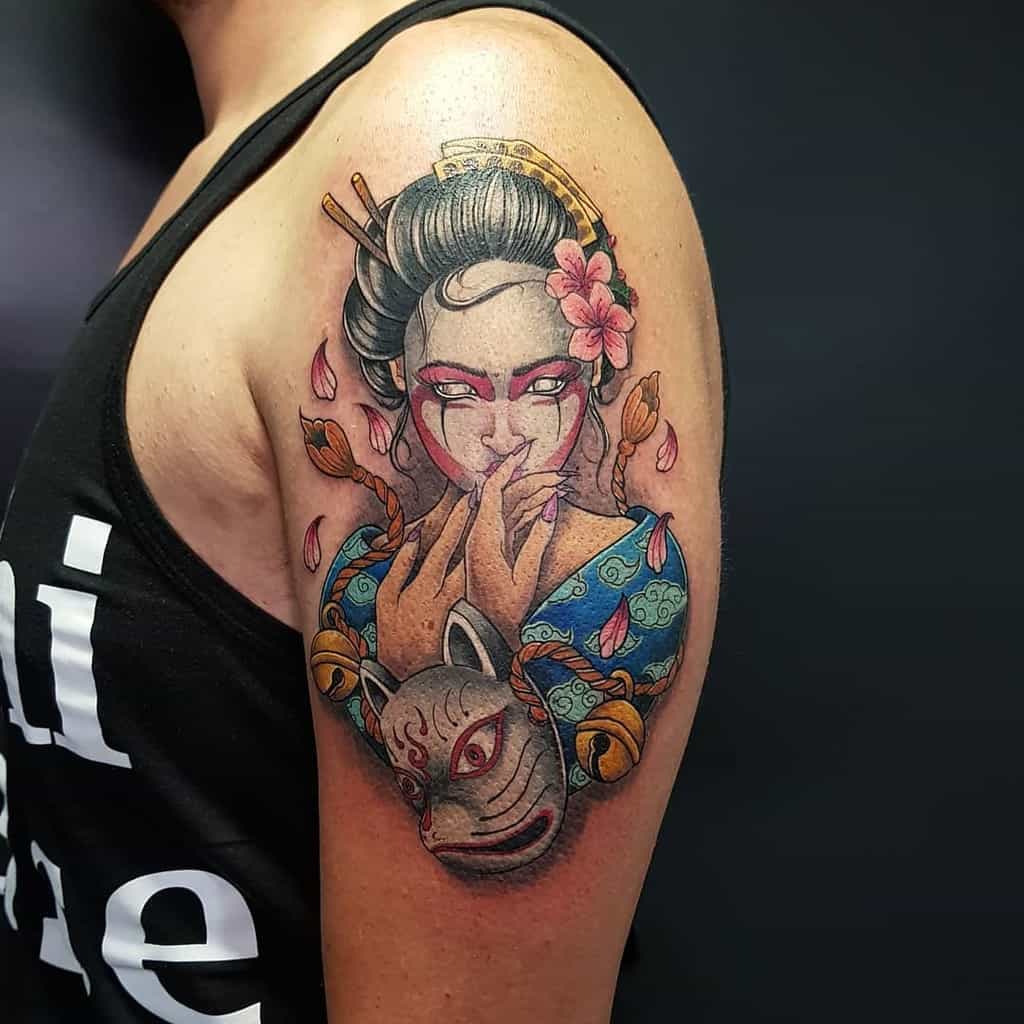 Vibrant upper arm tattoo of a Geisha with glowing red eyes, a floral hairpiece, intricate kimono details, and a kitsune mask surrounded by falling petals.