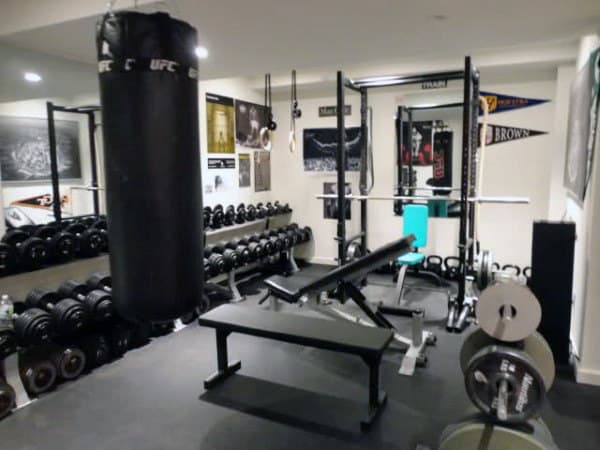 Home gym with weights, a home punching bag, bench press, and fitness gear in a room with sports decor