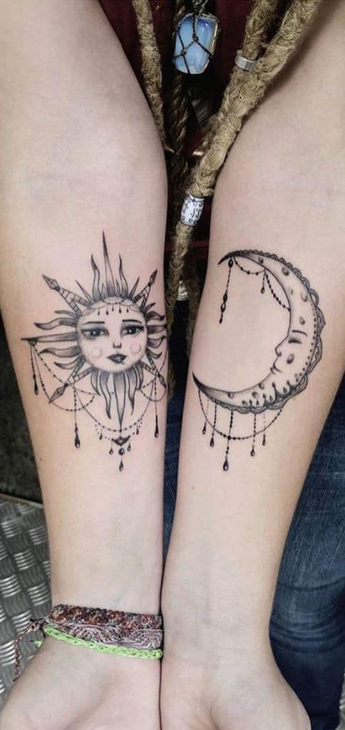 Matching black and grey tattoos of a celestial sun and crescent moon with delicate facial details and hanging ornaments on the forearms.