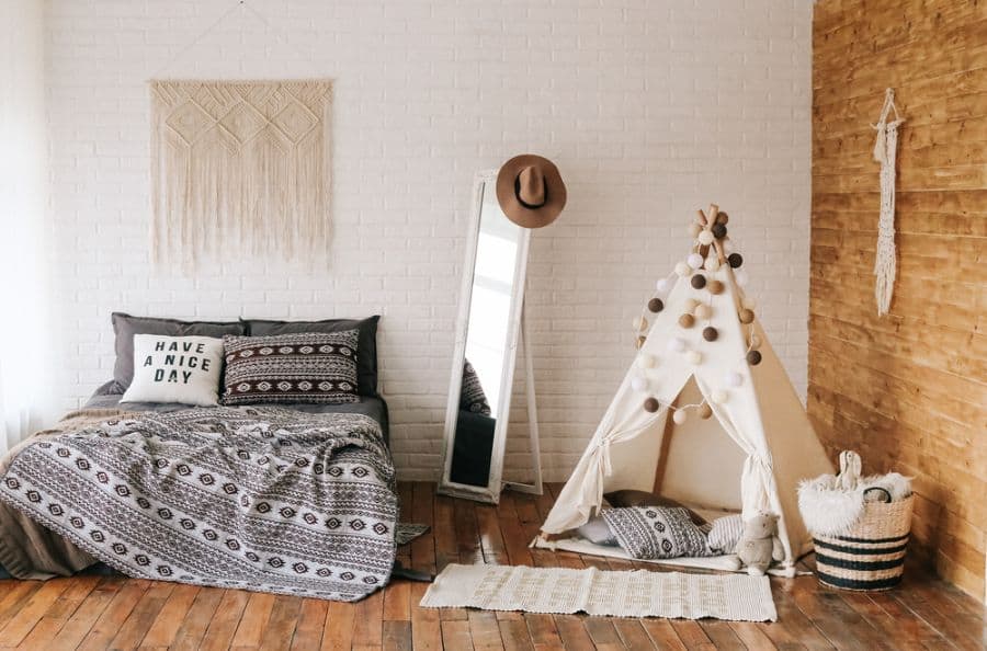 Boho bedroom with patterned bedding, teepee tent, tall mirror, and macrame wall decor.