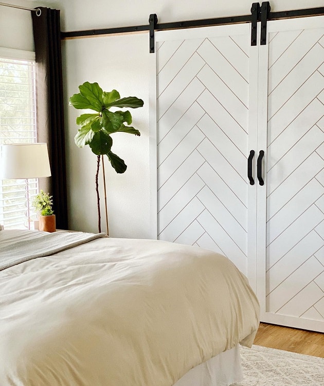 White sliding barn doors with a chevron pattern in a boho chic bedroom featuring a fiddle-leaf fig plant.
