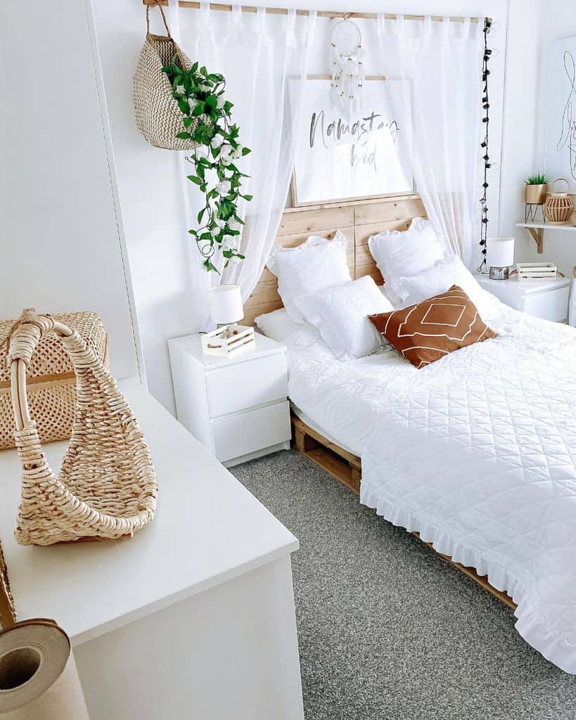 Bright bedroom with white bedding, wooden headboard, dreamcatcher, and hanging plants for a cozy, bohemian vibe