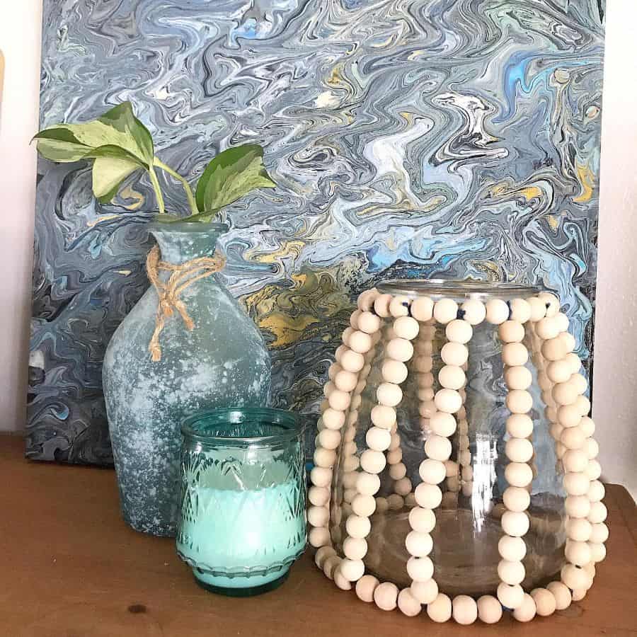 Boho decor with marbled art, glass vases, and a beaded candle holder on a wooden surface.