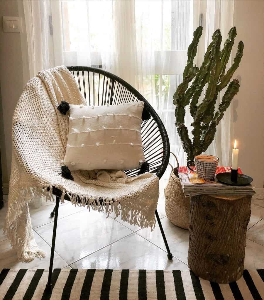 Cozy boho corner with a woven chair, neutral throw, cactus, and a log side table with a candle.