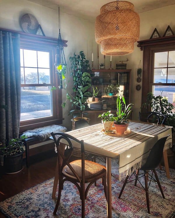 Boho-style dining room with patterned curtains, woven lighting, lush greenery, and wooden furniture.