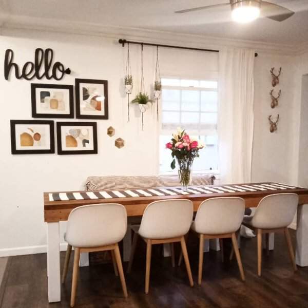 Boho-style dining room with white curtains, a wooden table, modern chairs, and hanging planters.