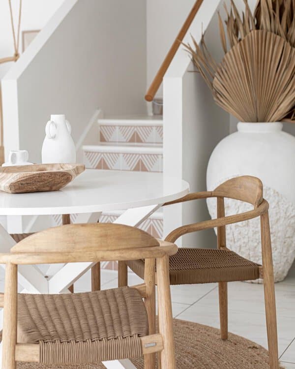 Minimalist boho dining area with a white round table, woven wooden chairs, and earthy decor.