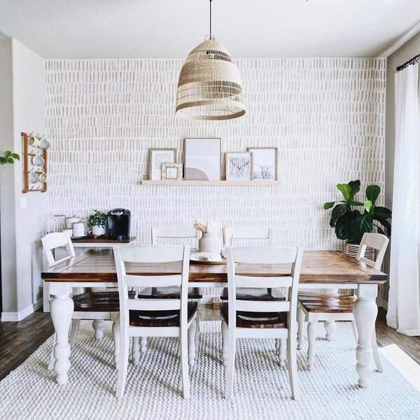 Boho dining room with a rustic wooden table, white chairs, and a woven pendant light.