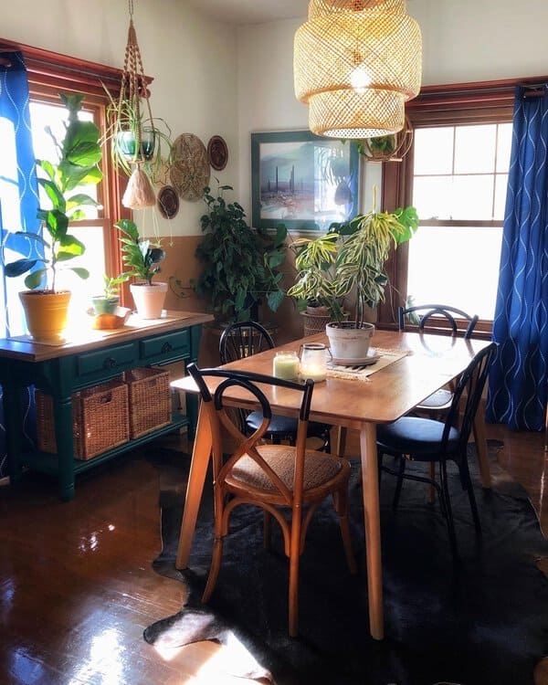 A cozy boho dining area with a wooden table, black and natural chairs, and abundant indoor plants, highlighted by a woven pendant light.