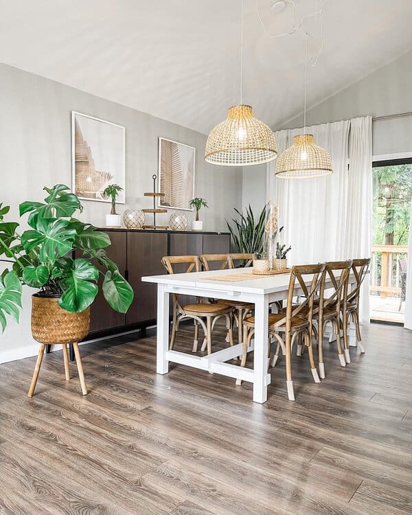 Boho dining room with a white table, wooden chairs, woven pendant lights, and lush plants.