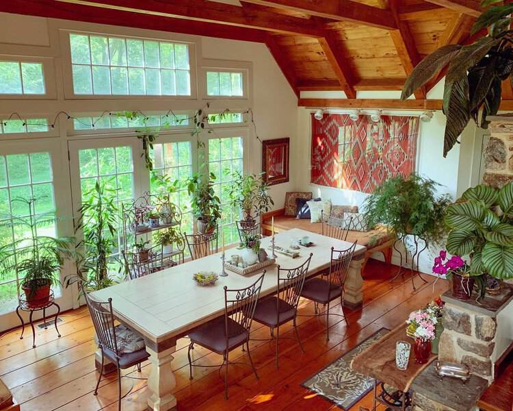 Boho dining room with a wooden table, metal chairs, and lush plants by large windows.