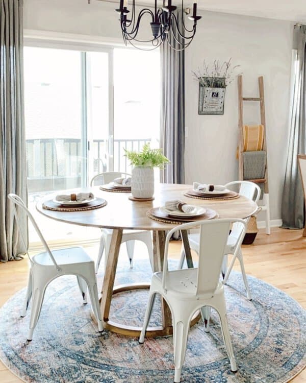 Boho dining room with a round wooden table, white metal chairs, and a vintage rug.