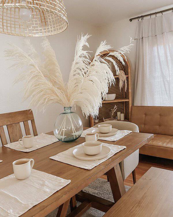 Boho dining room with neutral shades, wooden table, and pampas grass centerpiece.