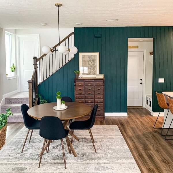 Boho dining room with a round wooden table, black chairs, and deep green accent walls.