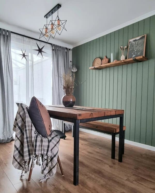 Boho dining room with a rustic wood table, green paneled walls, and geometric lighting.