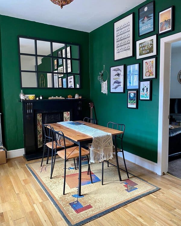 Boho dining room with deep green walls, a wooden table, and eclectic wall art.
