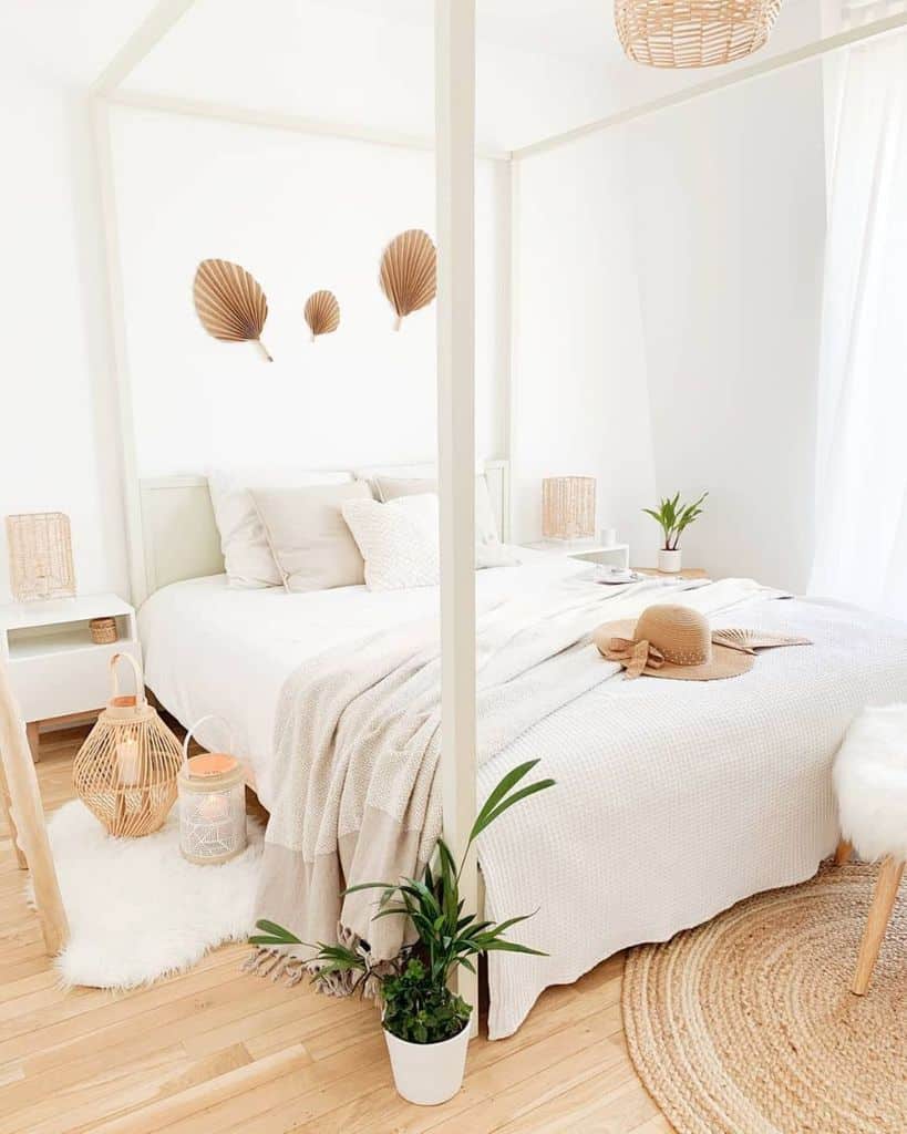 White bedroom with a canopy bed, wicker accents, leafy plants on wooden floors, and minimalist decor
