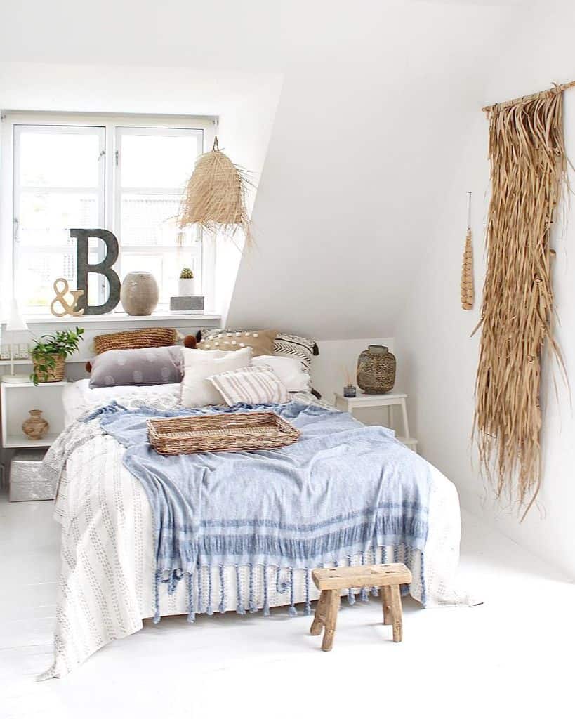 Bright bedroom with blue and white accents, rustic decor, and natural light. Wall art and woven elements add coziness