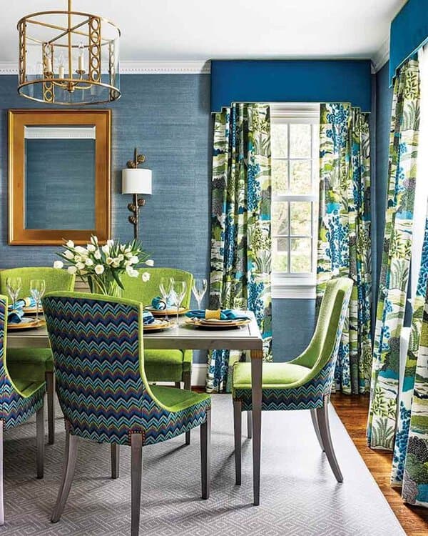Vibrant dining room with bold patterned curtains, green and blue chairs, and a gold chandelier.