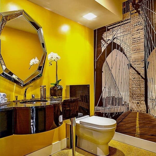 A bright yellow bathroom with a large bridge mural, mirrored vanity, and an orchid on the counter.