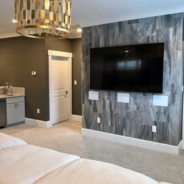Modern lounge with large wall-mounted TV, gray textured wall, mini bar, and gold chandelier.