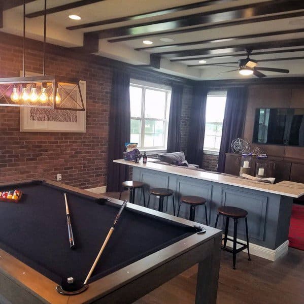 Stylish game room with pool table, home bar, brick accent wall, and modern lighting.