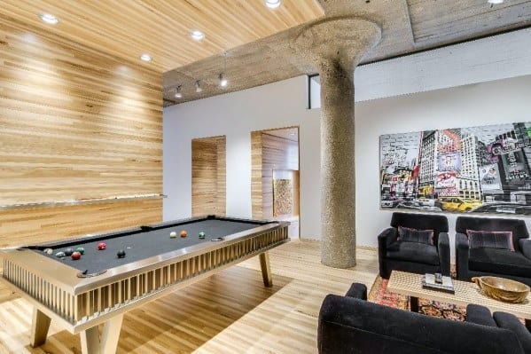 Modern game room with sleek pool table, black chairs, wood panel walls, and urban artwork.