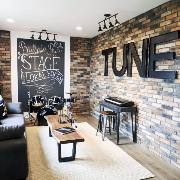 Cozy music room with drum set, keyboard, sofa, and brick wall decor featuring TUNE sign.