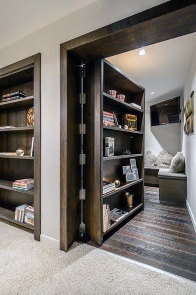 A hidden room accessed through a rotating bookshelf, revealing a cozy seating area with cushions and shelves