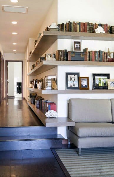 Hallway with bookshelves, framed photos, and a gray sofa on dark hardwood floors