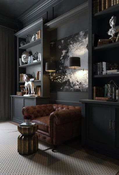 A cozy, dark bookcase setup with leather seating, modern lighting, decorative sculptures, and a sophisticated, artistic ambiance